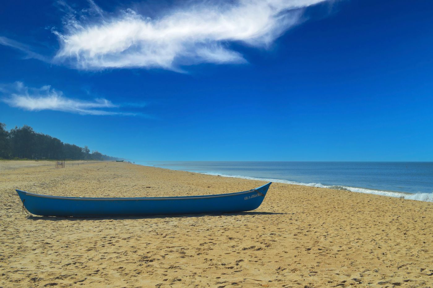 A tranquil sandy beach in Karnataka, India, featuring a blue canoe under a clear blue sky.